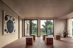 A minimalist living room features clay-tiled flooring, large windows, and a simple, modern decor.