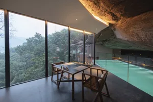 Modern luxury resort dining room with glass walls overlooking a scenic poolside and natural landscape.