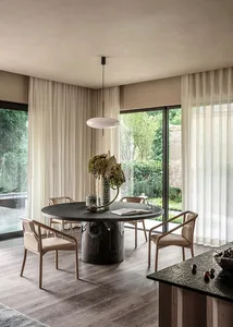 A modern minimalist dining room with a round table, wood chairs, and a hanging pendant light.