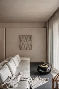 A modern minimalist living room featuring a white sofa with cushions, a black round coffee table, and a geometric wall art pi