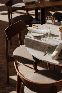 Modern restaurant table setting with white tiles, fabric upholstered chairs, white tableware, and minimalistic design element