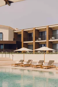 Swimming pool area featuring modern residential architecture with wooden sun loungers, concrete steps, and lush greenery.