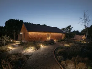 A wooden house with bamboo elements illuminated at night, featuring a curved pathway and surrounding garden.