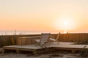 A minimalist wooden pavilion overlooking the ocean during sunset.