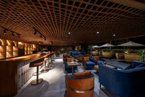 Modern bar lounge area with a wooden lattice ceiling, concrete bar countertop, and comfortable seating arrangements.