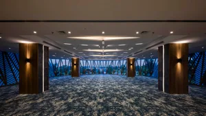 Modern, carpeted conference hall interior with large windows showing outdoor scenery.