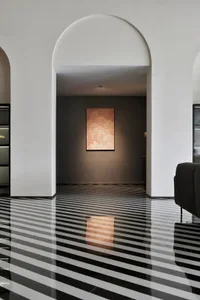 A modern living room with a striped tile floor and an archway leading to a darker room with a lit artwork.