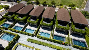 Aerial view of modern residential homes with private pools surrounded by greenery and terraced roofs.