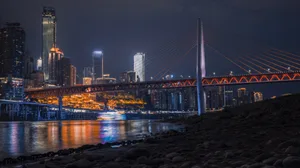 A nighttime cityscape featuring a illuminated bridge with reflections in a body of water.