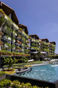Modern apartment building exterior with balconies featuring hanging plants and a swimming pool.