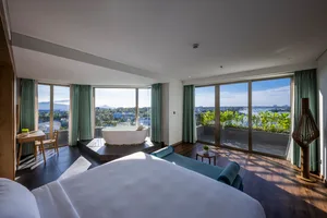 Modern bedroom with black flooring, leather seating, and floor-to-ceiling windows overlooking a scenic view.
