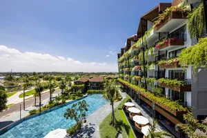 A modern hotel with concrete and glass exteriors, featuring a large pool area and lush greenery.