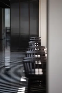A row of wooden dining chairs arranged in a restaurant interior. The chairs have a minimalist design and are set against a sl