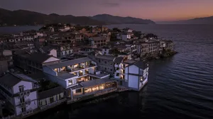 Aerial view of a beachside villa at dusk, featuring traditional architectural elements, illuminated windows, and a serene wat