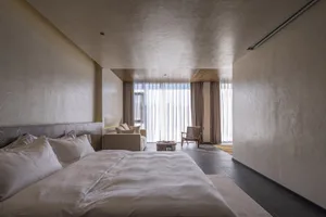 A minimalist bedroom with textured walls, a large window, and white bedding.