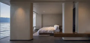 A minimalist bedroom with concrete walls and floor, featuring a bed with white bedding and wooden accents.