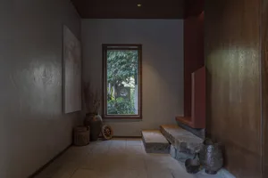 Corridor with concrete walls, stone steps, and stone containers, featuring a window with trees visible outside.