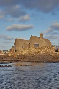 A modern house built on a rocky cliff with concrete walls and a large window.