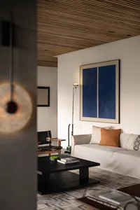 Modern living room with a white sofa, brown accent pillow, and a large blue abstract painting on the wall. Wooden accents and