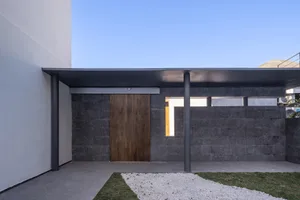 Modern minimalist exterior with concrete walls, a wooden door, and a gravel courtyard.