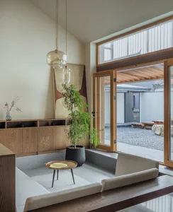 A minimalist living room with wooden furniture and elements, featuring a large window and a potted plant.