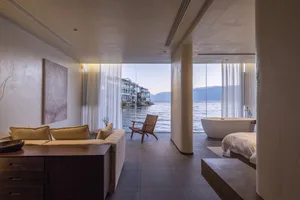 A modern residential bedroom featuring minimalist design with concrete floor, glass walls, and a serene view of the ocean.