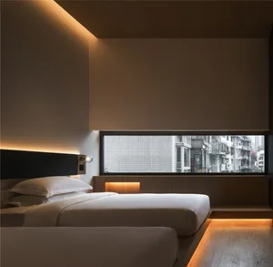 A minimalist hotel room with a small window, wooden flooring, and glass walls.