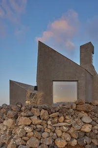 A modern house made of concrete and glass with a sloped roof and a window on the side.