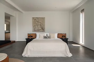 A minimalist bedroom with a concrete floor, a large bed, and a single abstract art piece on the wall.