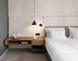 A minimalist hotel room features a concrete floor, white linens, and simple furnishings.