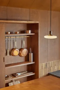 A modern minimalist kitchen with wooden cabinets, shelves, and utensils hanging on hooks.