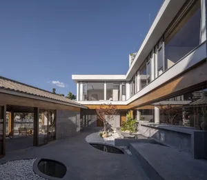 A modern residential exterior with concrete walls, glass windows, and a landscaped courtyard
