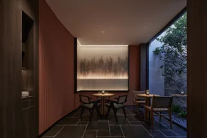 Circular table with chairs in a modern restaurant setting with a water feature and outdoor garden view.