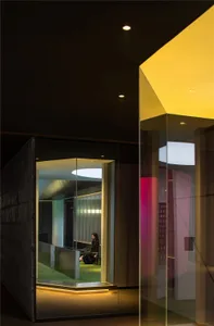 Modern minimalist office space with glass walls and concrete features, illuminated by LED lighting.