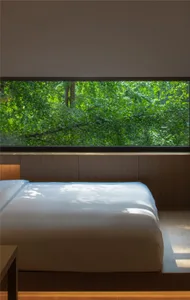 Modern bedroom with a zen-like atmosphere, featuring a bed surrounded by wooden walls and a large window with a view of lush 