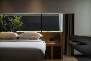 A minimalist bedroom with a wooden bed, white bedding, and a glass window with a tree outside.