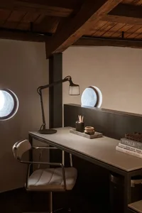 A modern, industrial home office featuring a concrete desk, metal lamp, and round windows.