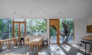 A minimalist cafe interior featuring glass walls, wooden tables, and concrete flooring.