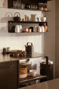 A minimalist residential kitchen featuring metal surfaces, white tiles, and organized shelving.