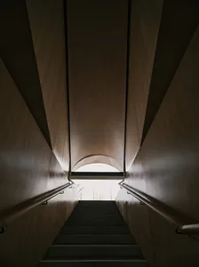 View looking up inside a modern, industrial tunnel with concrete walls and a natural light source at the end.