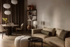 A modern living room with neutral tones, featuring a couch, round table, and bookshelf.