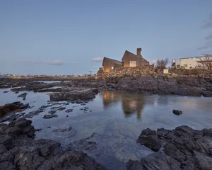 A modern residential building constructed of stone, situated on a rocky riverbank.