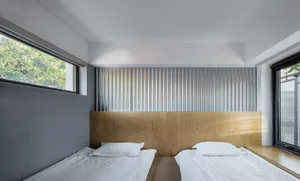 Minimalist bedroom featuring a corrugated metal headboard and twin beds with white linens.