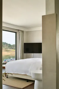 A minimalist bedroom with white bedding, concrete flooring, and a sleek glass and metal frame bed.