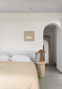 A minimalist bedroom with neutral-toned bedding and a wooden side table with a lamp.