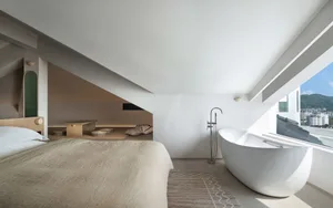 Modern minimalist bedroom with white concrete walls and floor, large window with city view.