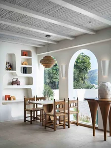 A minimalist dining room with concrete walls, wood furniture, and a modern chandelier.