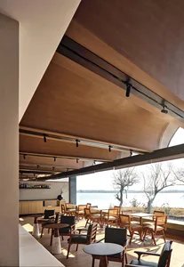 A minimalist restaurant with wooden furniture, glass windows, and concrete flooring and walls.