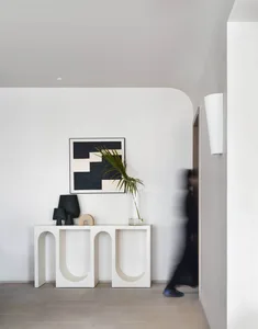 A minimalist entryway console table made of wood, featuring arch-shaped cutouts and a sleek, contemporary design, illuminated