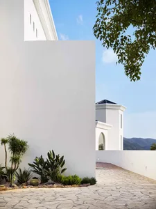 Modern exterior architectural space featuring concrete walls and a tiled pathway with greenery and a mountainous backdrop.